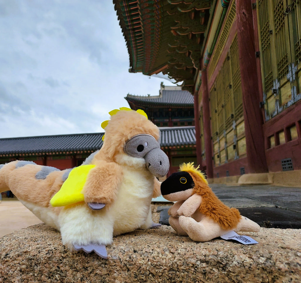 A large Utahraptor dinosaur plush sits next to a smaller one at a castle in Korea