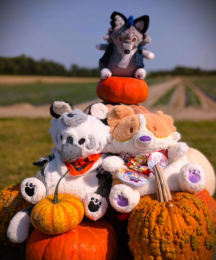 Plush backpacks of a gryphon and a red border collie sitting in some pumpkins with a werewolf plushie