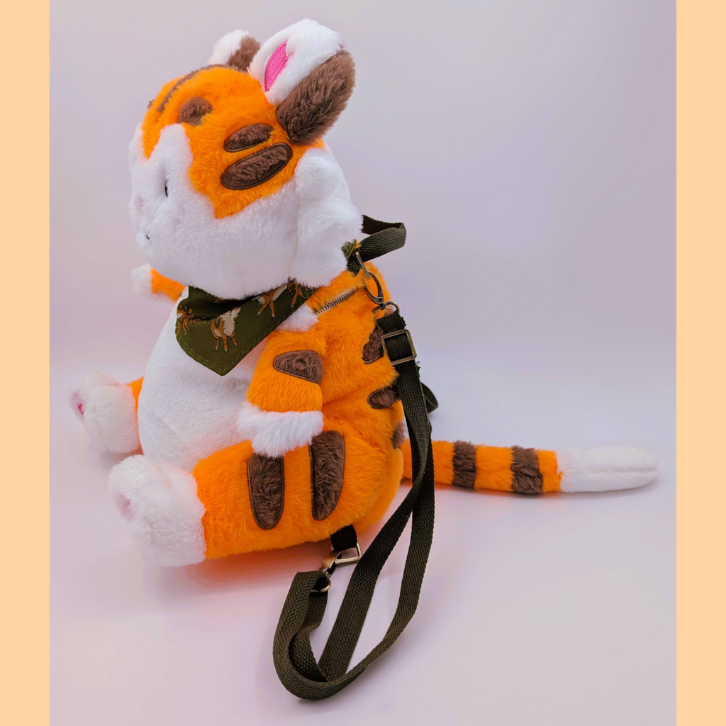 Side view of a plush backpack tiger with an orange and white body, brown accents, and a green bandana on a white background