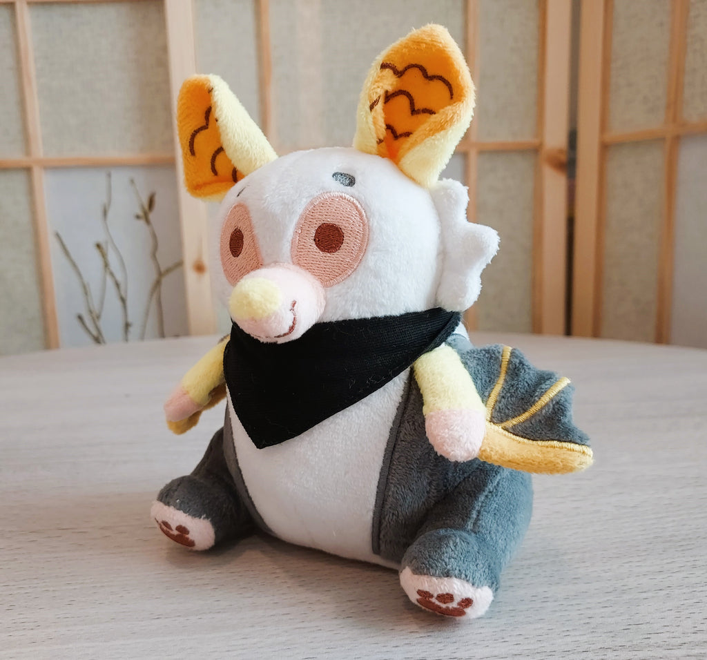 Beanie plush of lemon the yellow-eared bat wearing a black bandana