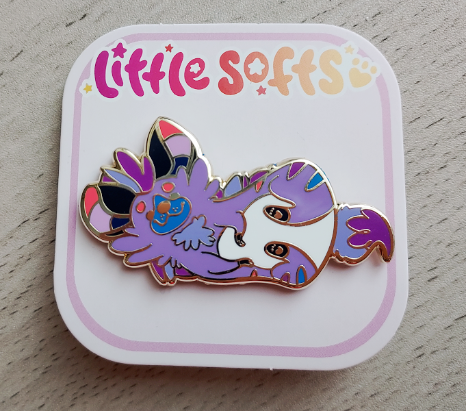 Enamel pin of Berry the purple, blue, and pink striped hyena lying down