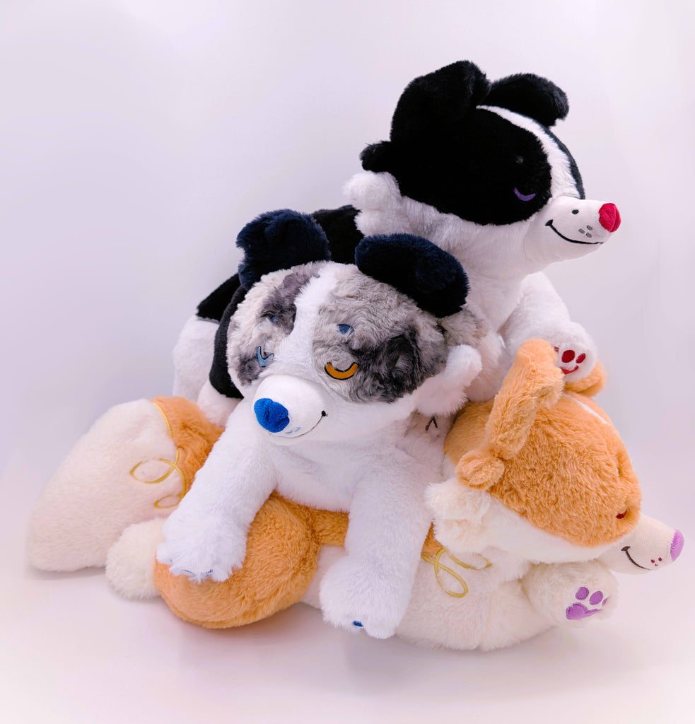 Three border collie plush toys, one red collie, one blue merle, and one black and white, stacked on top of eachother