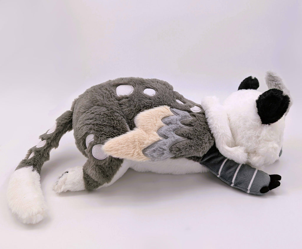 Side view of a weighted plush toy of Sesame the grey and white gryphon
