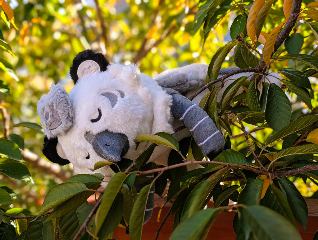 Weighted plush toy of Sesame the grey and white gryphon with his eyes closed, lying in a tree