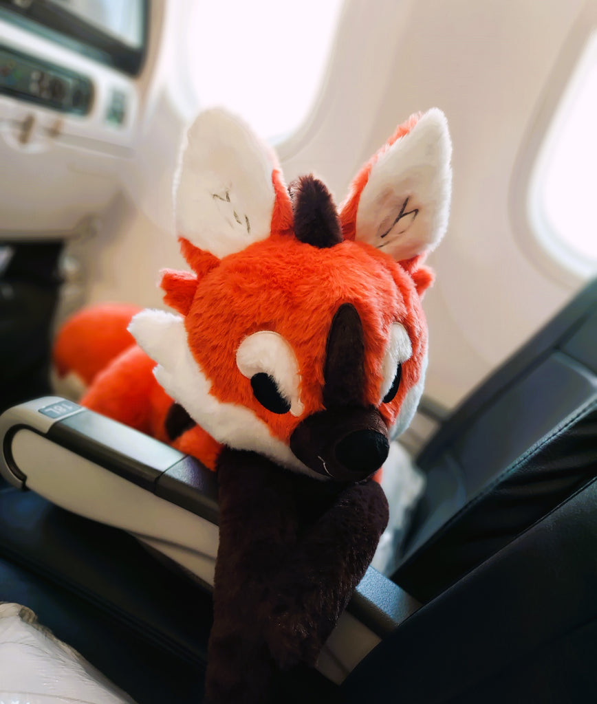 Plush toy of Paprika the maned wolf lying in an airplane seat