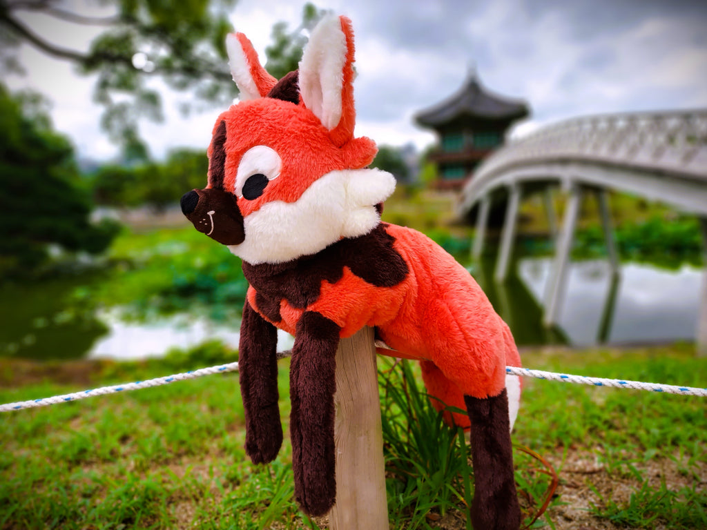 Plush toy of Paprika the maned wolf lying on a fence post