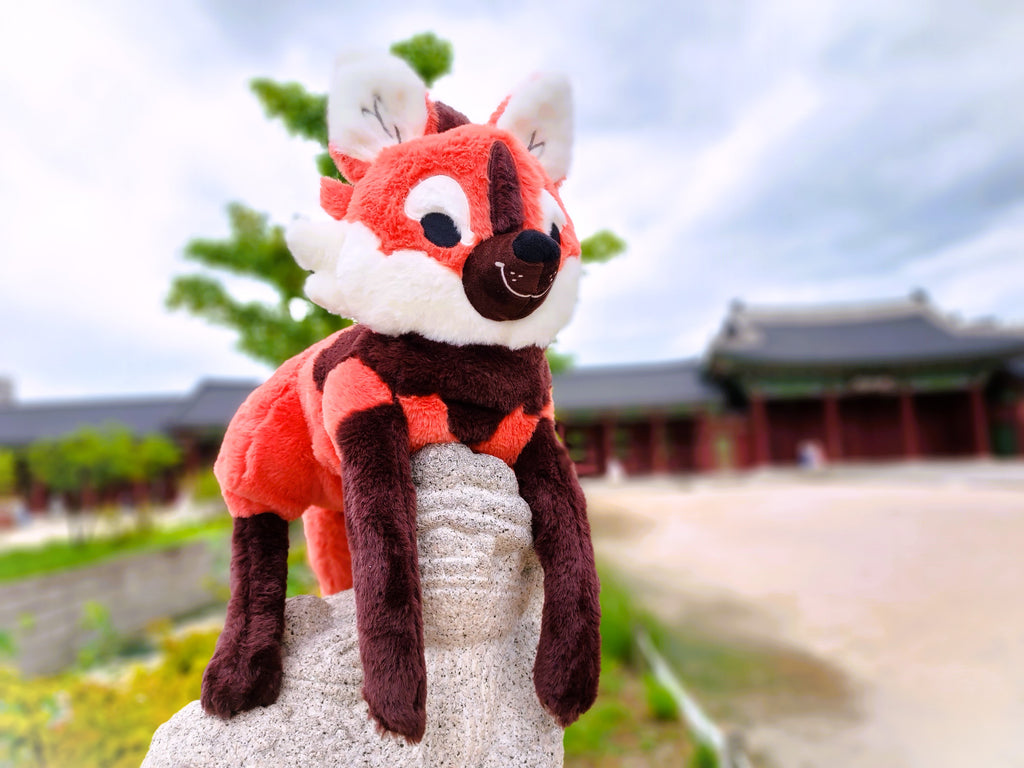 Plush toy of Paprika the maned wolf resting on a statue