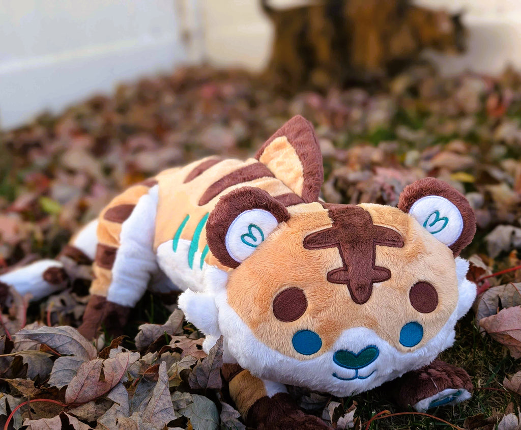 Plush toy of Cornflakes the Tiger and Shark hybrid lying in some fall leaves