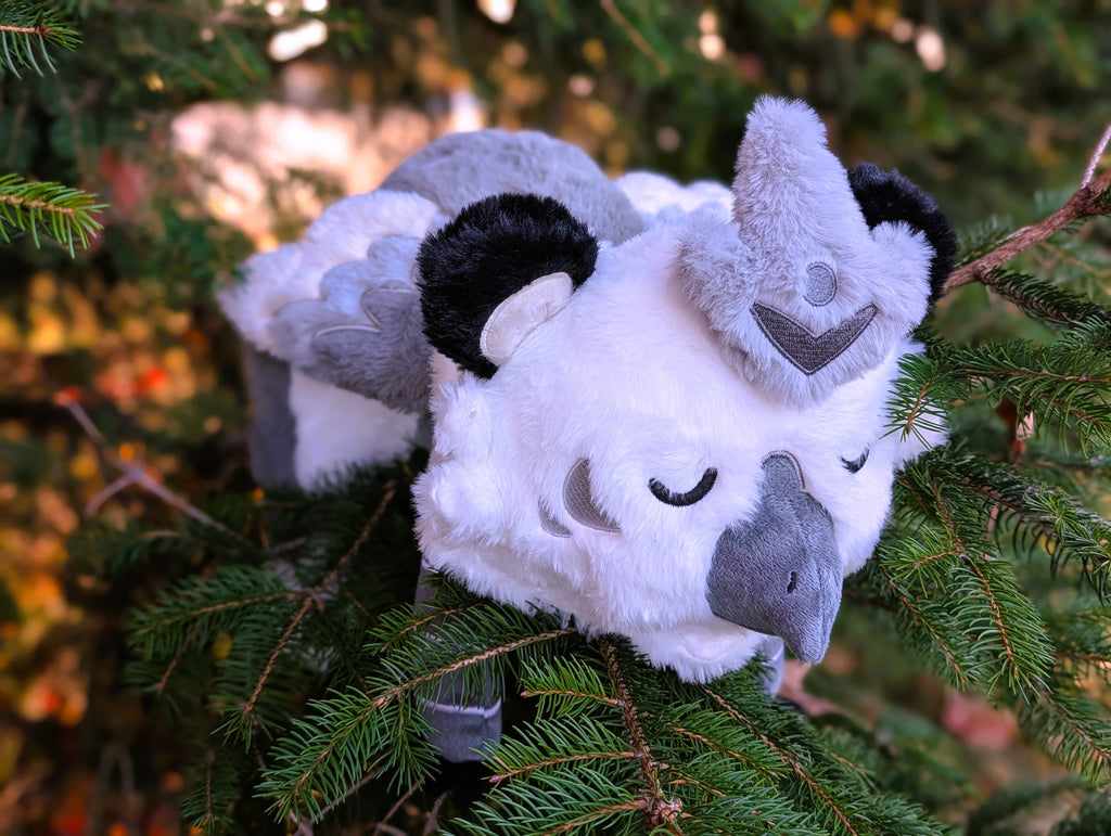 Plush toy of Sesame the grey and white gryphon resting in an evergreen tree