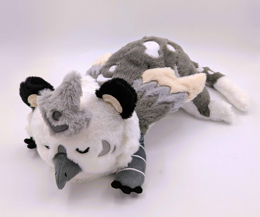 Weighted plush toy of Sesame the grey and white gryphon with his eyes closed 