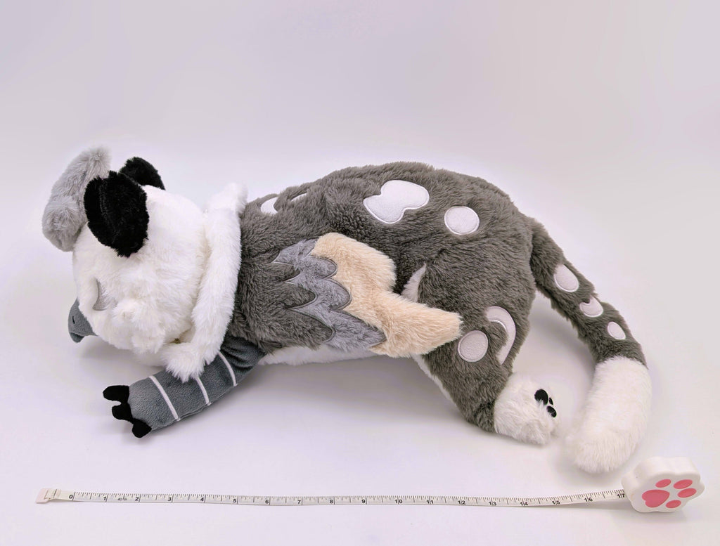 Side view of a weighted plush toy of Sesame the grey and white gryphon with a measuring tape
