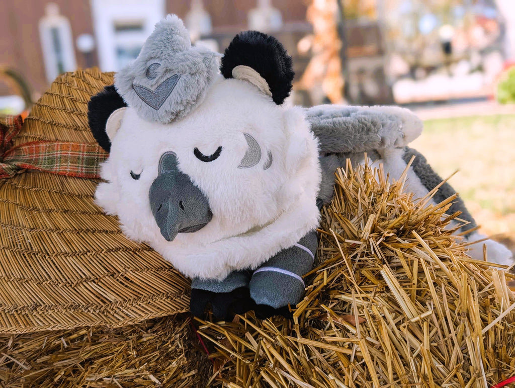 Plush toy of Sesame the grey and white gryphon resting in some straw