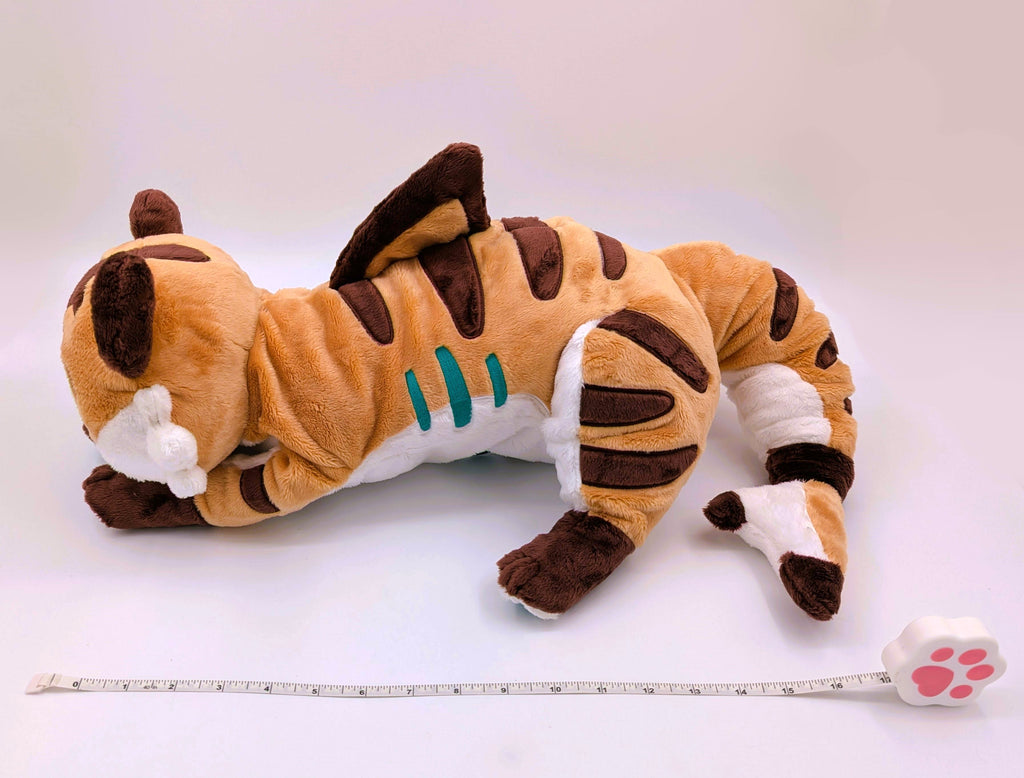 Side view of a plush of Cornflakes the Tiger and Shark hybrid, with a measuring tape 