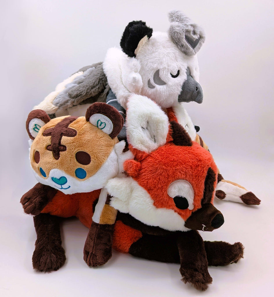 Plush toys of Paprika the maned wolf, Cornflakes the tiger and shark hybrid, and Sesame the grey and white gryphon, lying in a pile