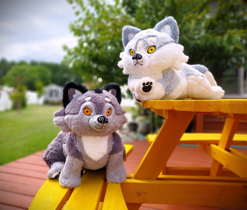 BigHugs weighted plush of Wolfgang the dark grey wolf and Biscuit the white wolf sitting on a yellow picnic bench