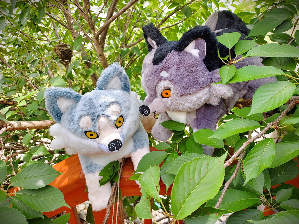 BigHugs weighted plush of Wolfgang the dark grey wolf and Biscuit the white wolf sitting in the trees