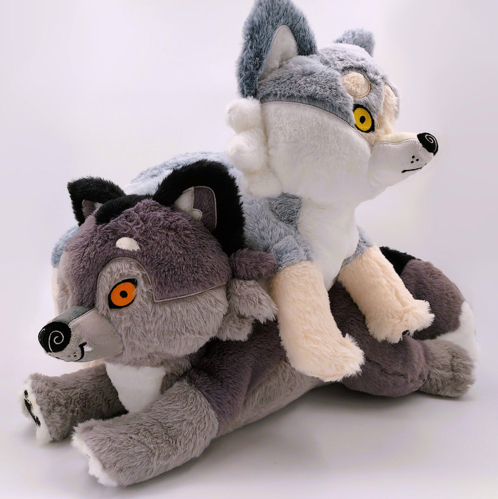 BigHugs weighted wolf pillow plush of Wolfgang the dark grey wolf and Biscuit the white wolf. Biscuit is laying on Wolfgang.