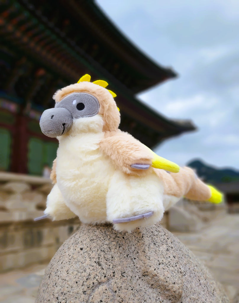 Plush toy of Chai Latte the utahraptor in front of a building in Asia