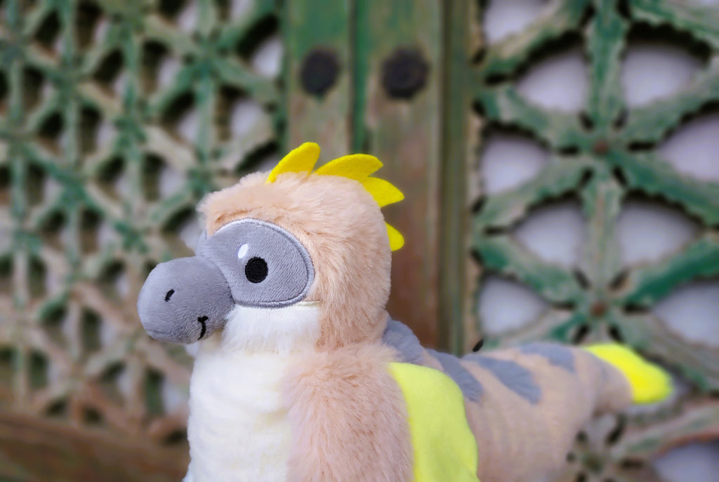 Plush toy of Chai Latte the utahraptor in front of a green lattice door