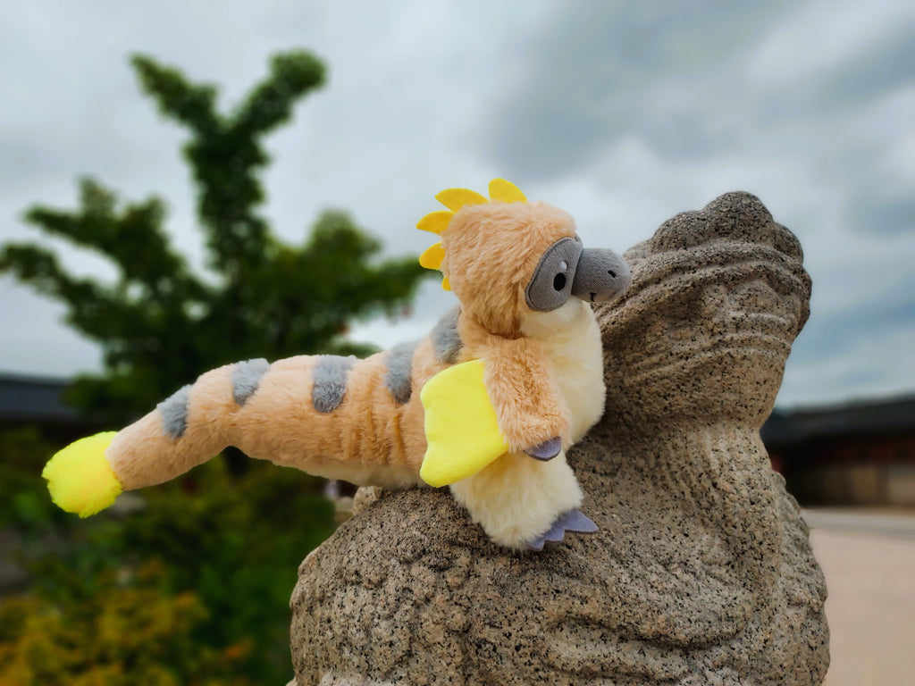 Plush toy of Chai Latte the utahraptor posing on a statue