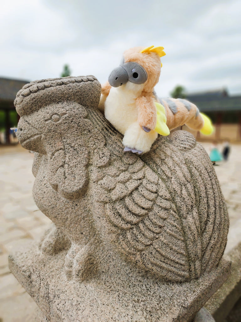 Plush toy of Chai Latte the utahraptor on a statue