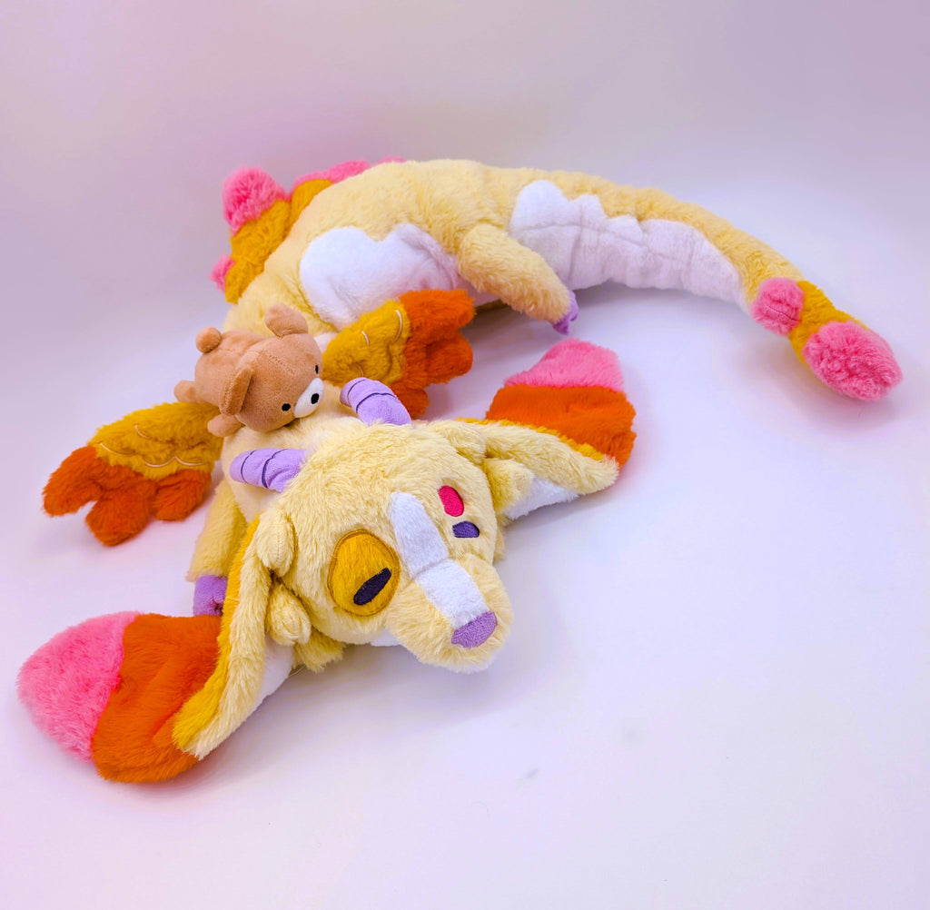Long pillow plush toy of Charmy the dragon who is pink, orange,yellow and has a brown bear toy on his head