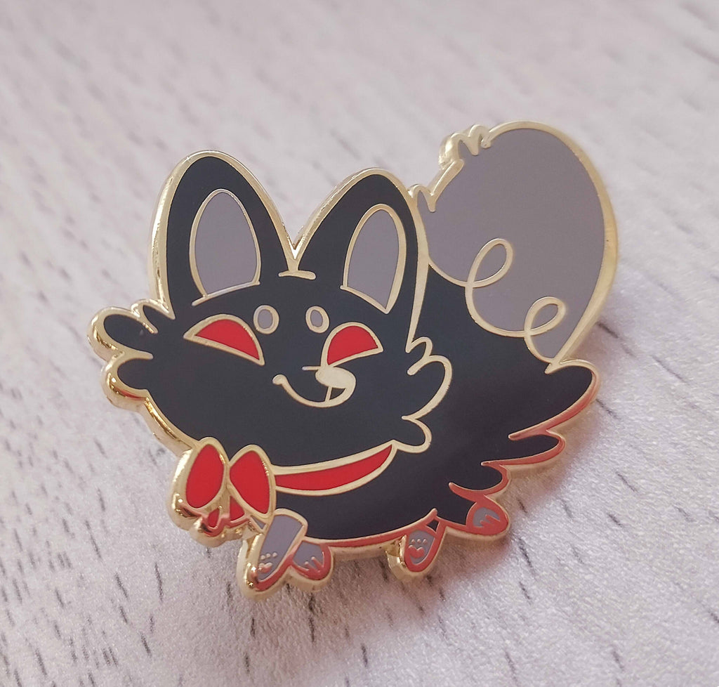 Enamel pin of Crafty Tricks the black fox, wearing a red ribbon