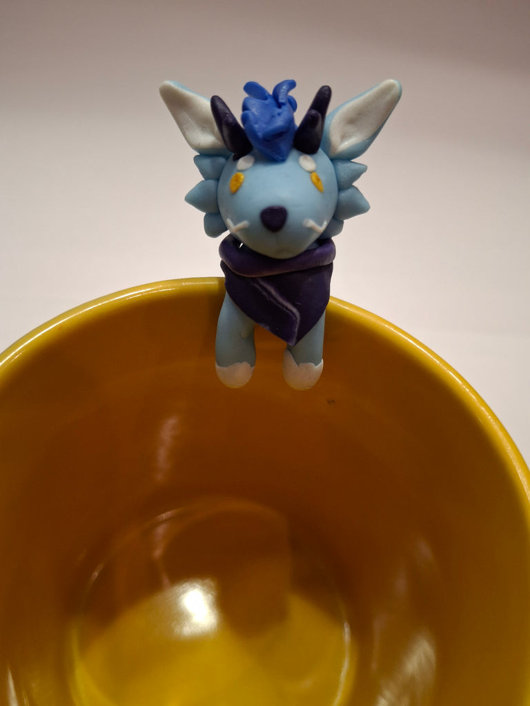 Sculpture of a blue dragon posed on a yellow mug