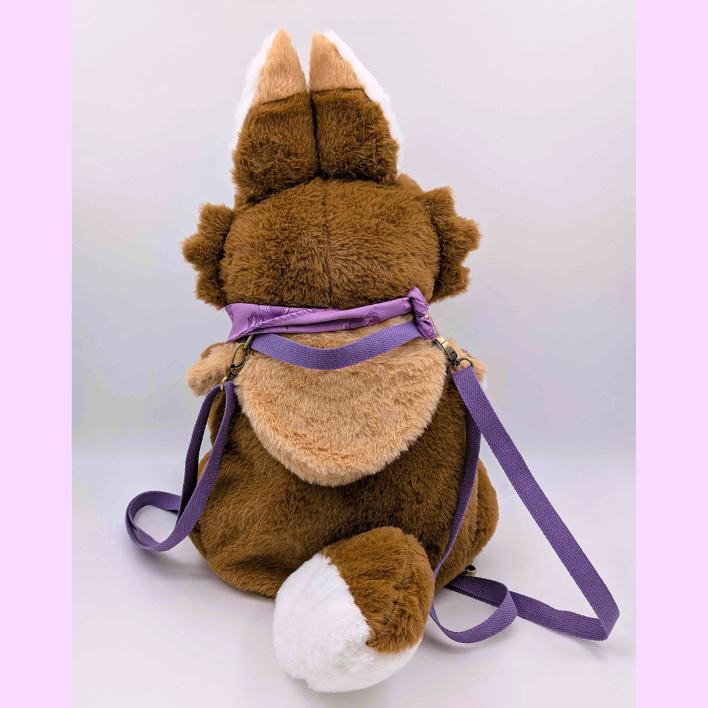 Back view of a brown plush backpack of a jackalope with purple straps on a white background