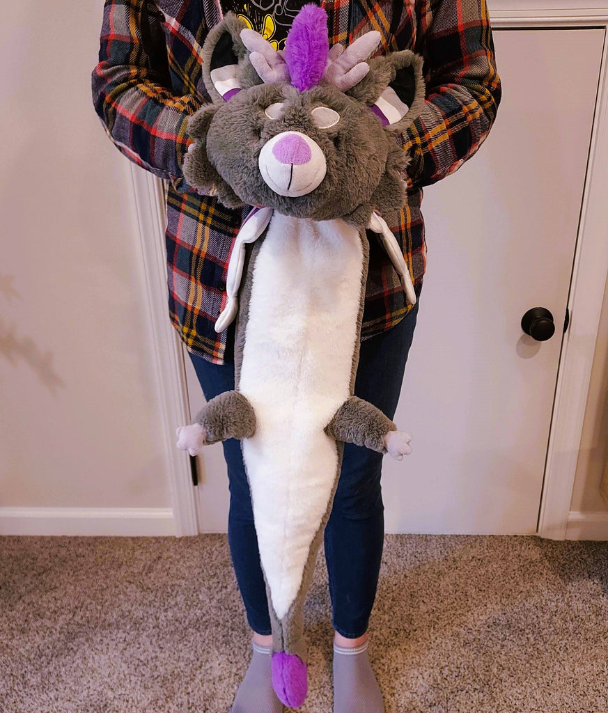 A person holding a large plush of Marshmallow the purple, black, white, and grey dragon. He is asleep.