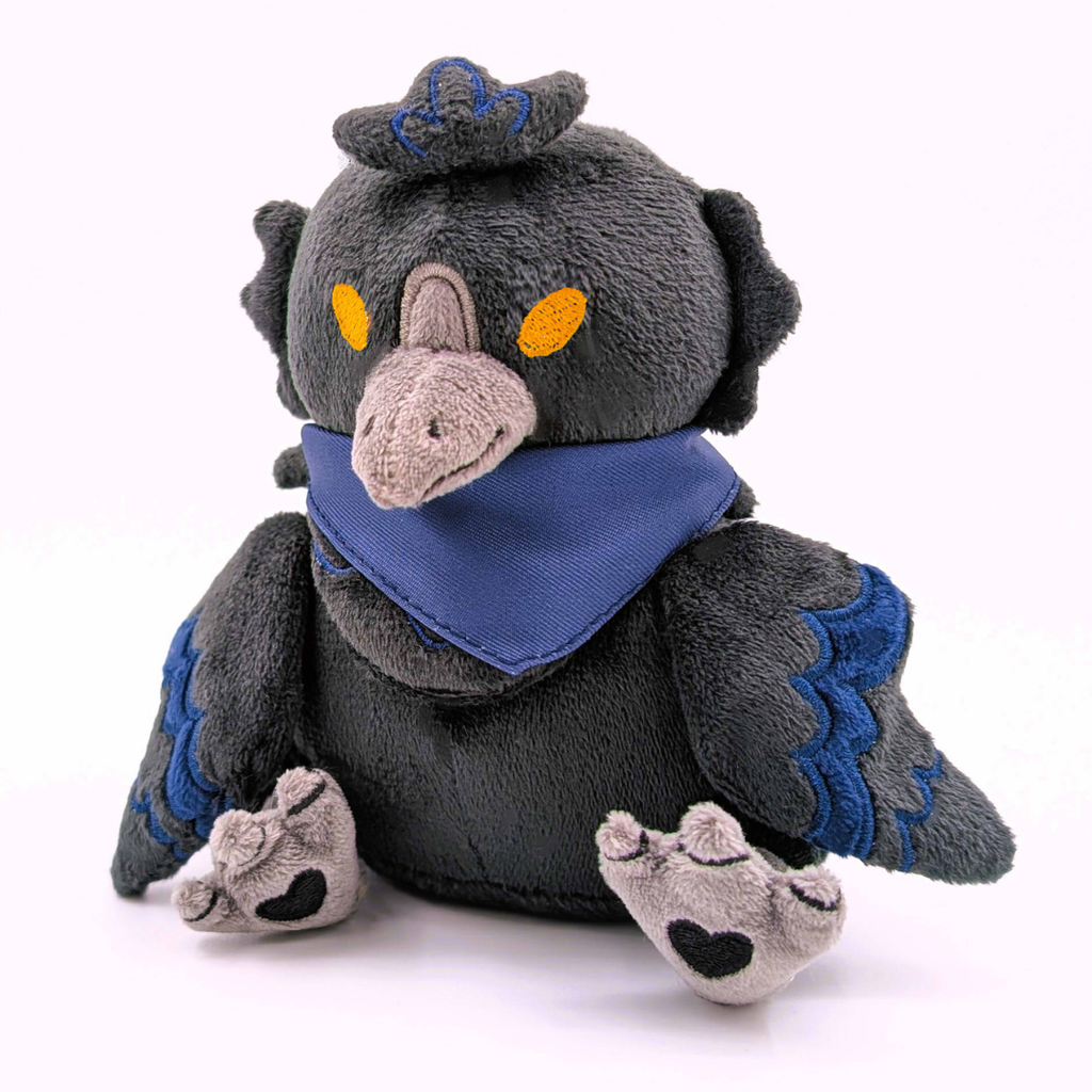 Plush toy of a raven with a dark gray body, blue accents, and orange eyes on a white background. He is wearing a blue bandana.
