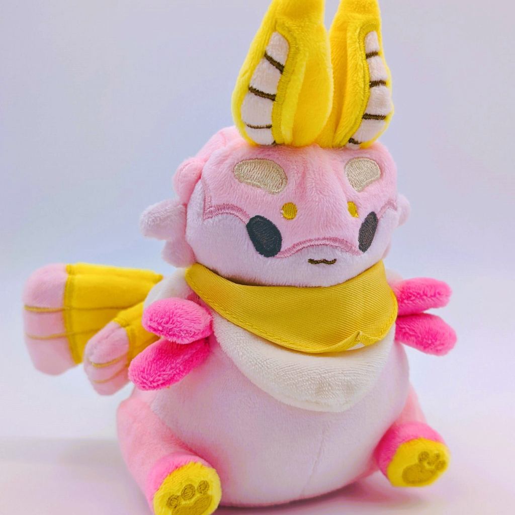 Pink plush toy of a moth with yellow accents on a white background