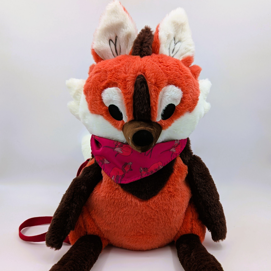 Plush toy maned wolf with a pink bandana on a white background