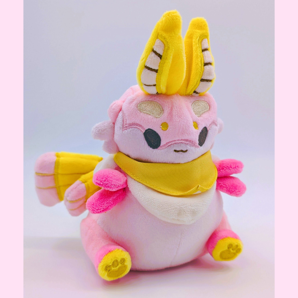 Pink plush toy of a moth with yellow accents on a white background
