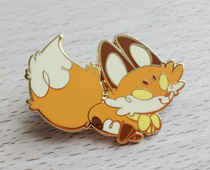 Enamel pin of a red fox with yellow eyes wearing a yellow bow