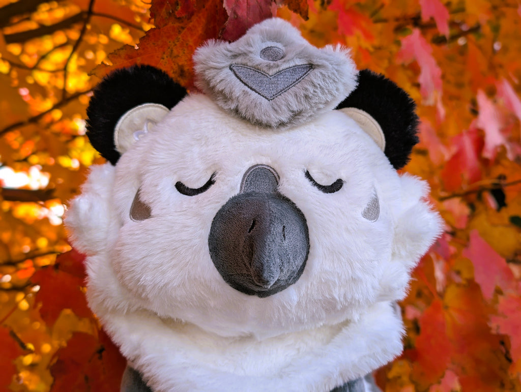 Plush toy of Sesame the grey and white gryphon with red fall leaves in the background