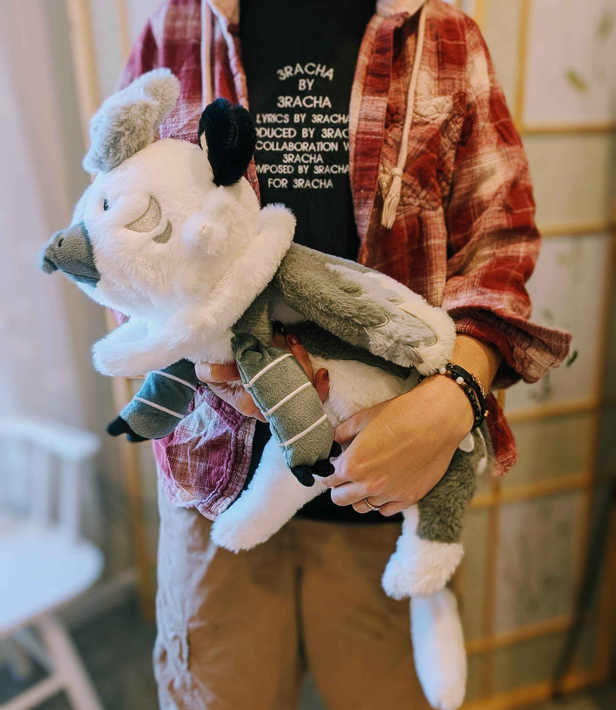 Plush toy of Sesame the grey and white gryphon being held by a person