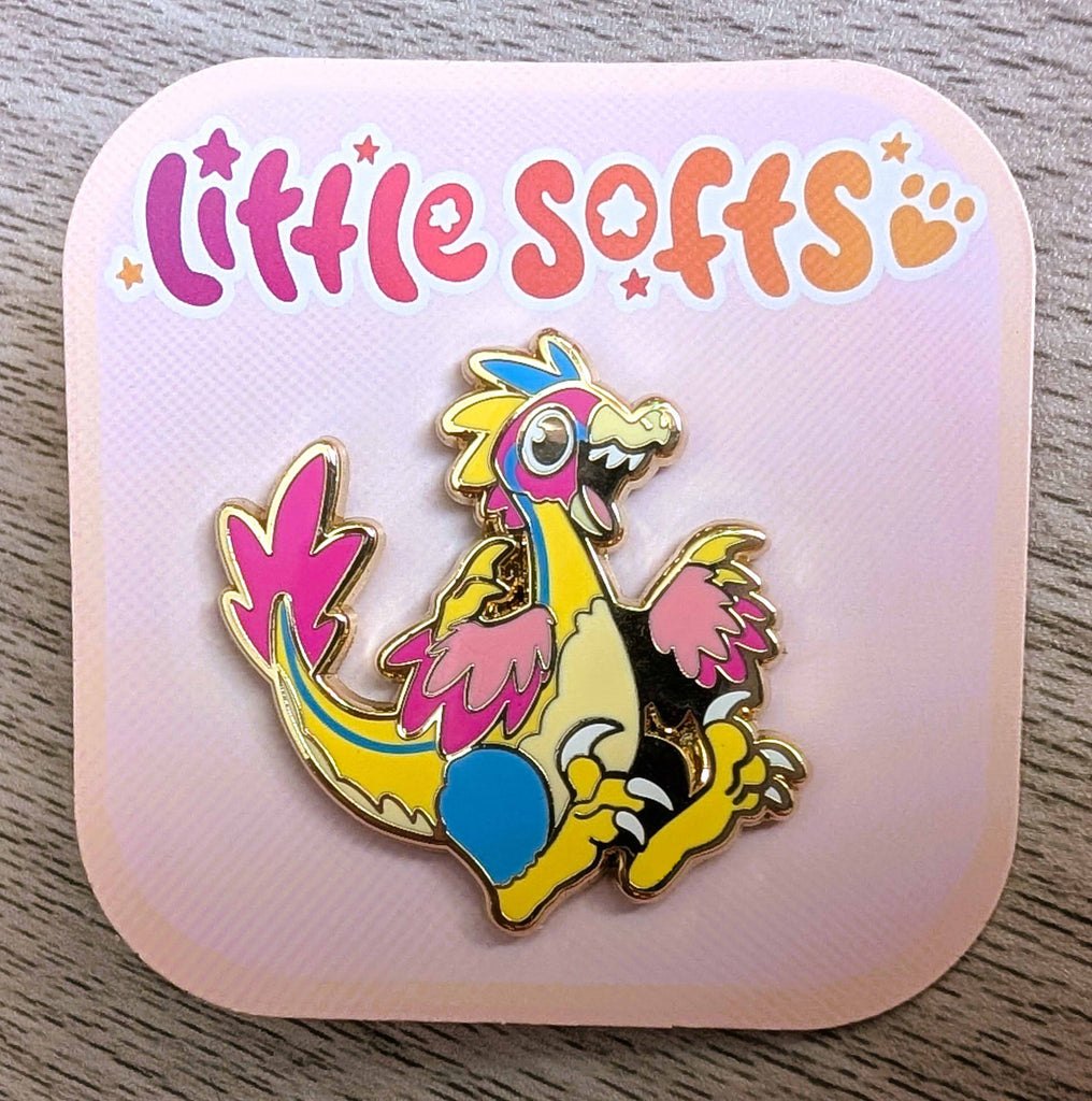 Enamel pin of Sherbert the rainbow utahraptor who is pink, yellow, and blue