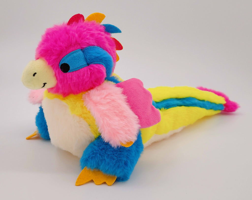 Plush toy of Sherbert the rainbow utahraptor who is pink, yellow, and blue