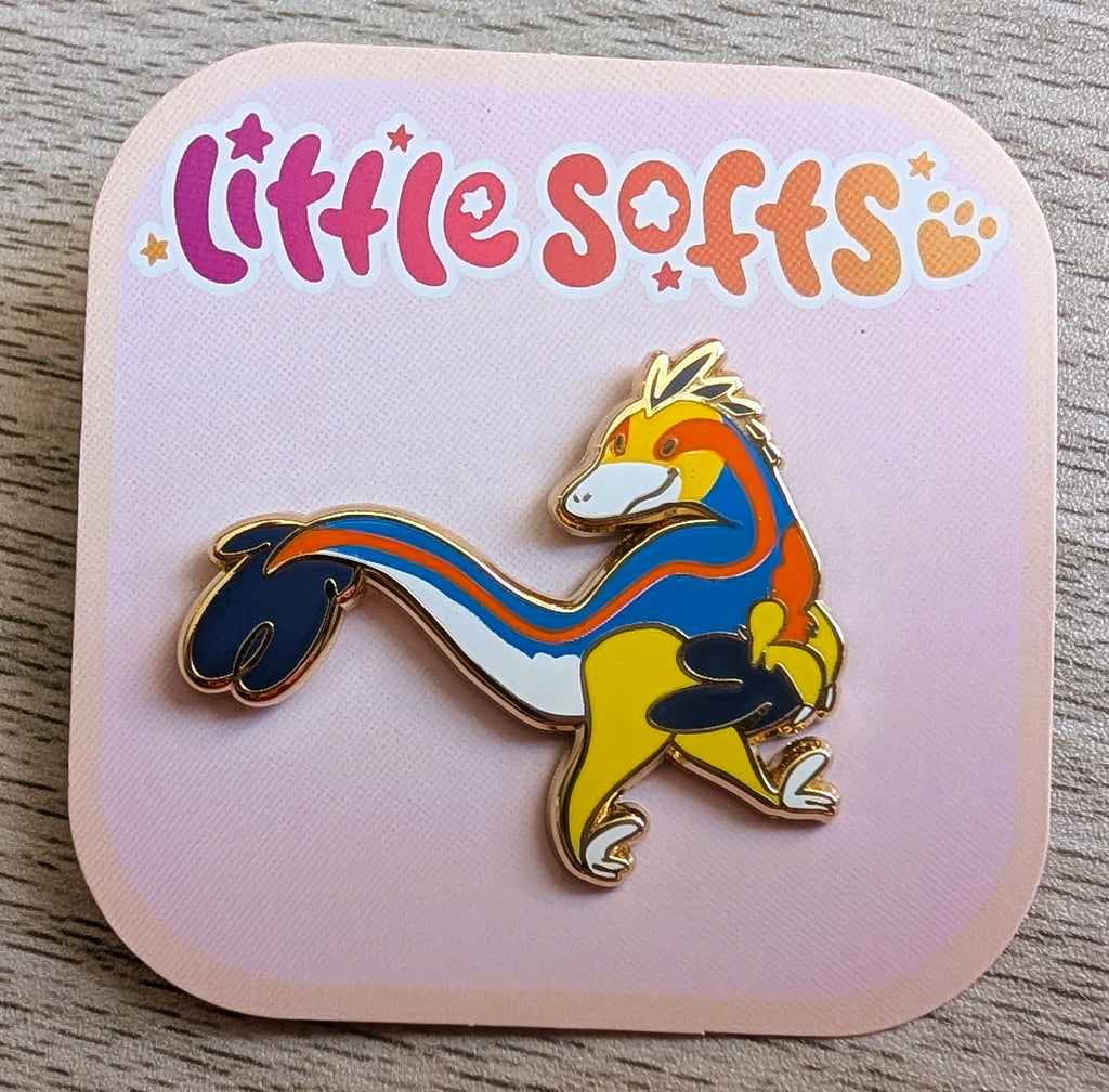 Enamel pin of Slushie the blue, orange, yellow, and white utahraptor