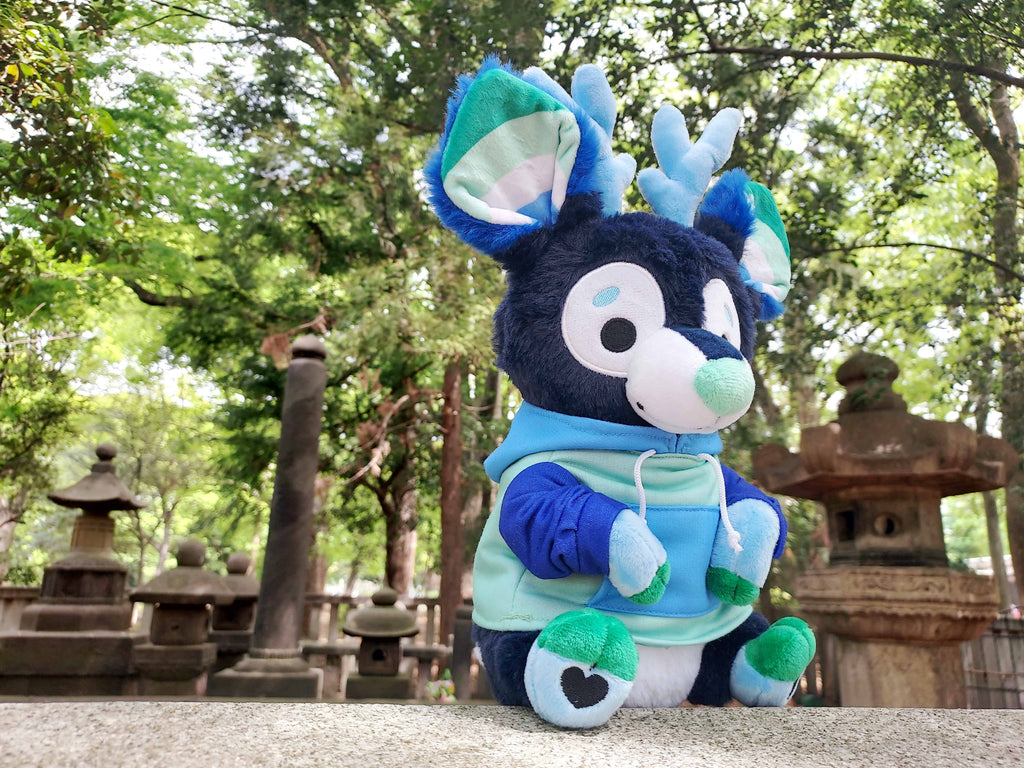 Plush toy of Smoothie the blue and green stag sitting at a shrine in Asia