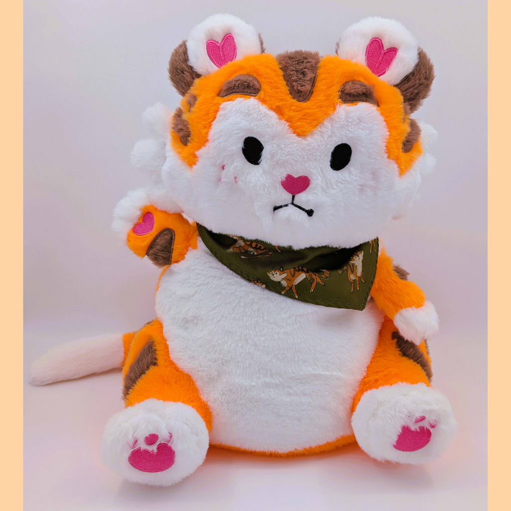 Plush toy tiger with an orange and white body, brown accents, and a green bandana on a light pink background.