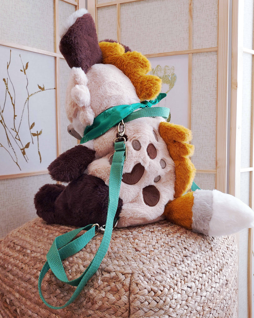 Side view of a plush backpack of Chocochip the hyena wearing a green bandana, with green backpack straps
