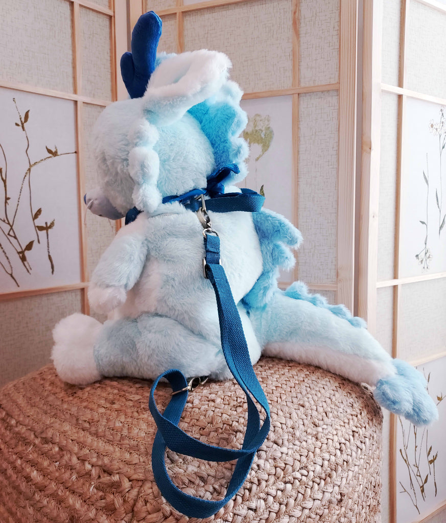 Side view of a plush backpack of Cloud the blue dragon wearing a blue bandana, with blue backpack straps
