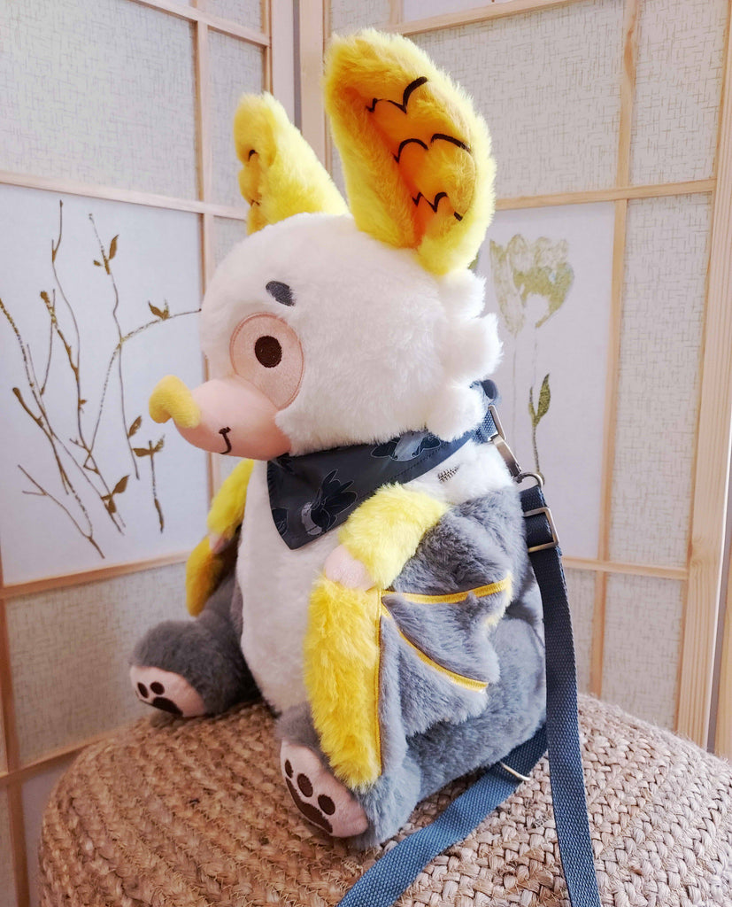 Side view of a plush backpack of Lemon the bat wearing a black bandana, with black backpack straps
