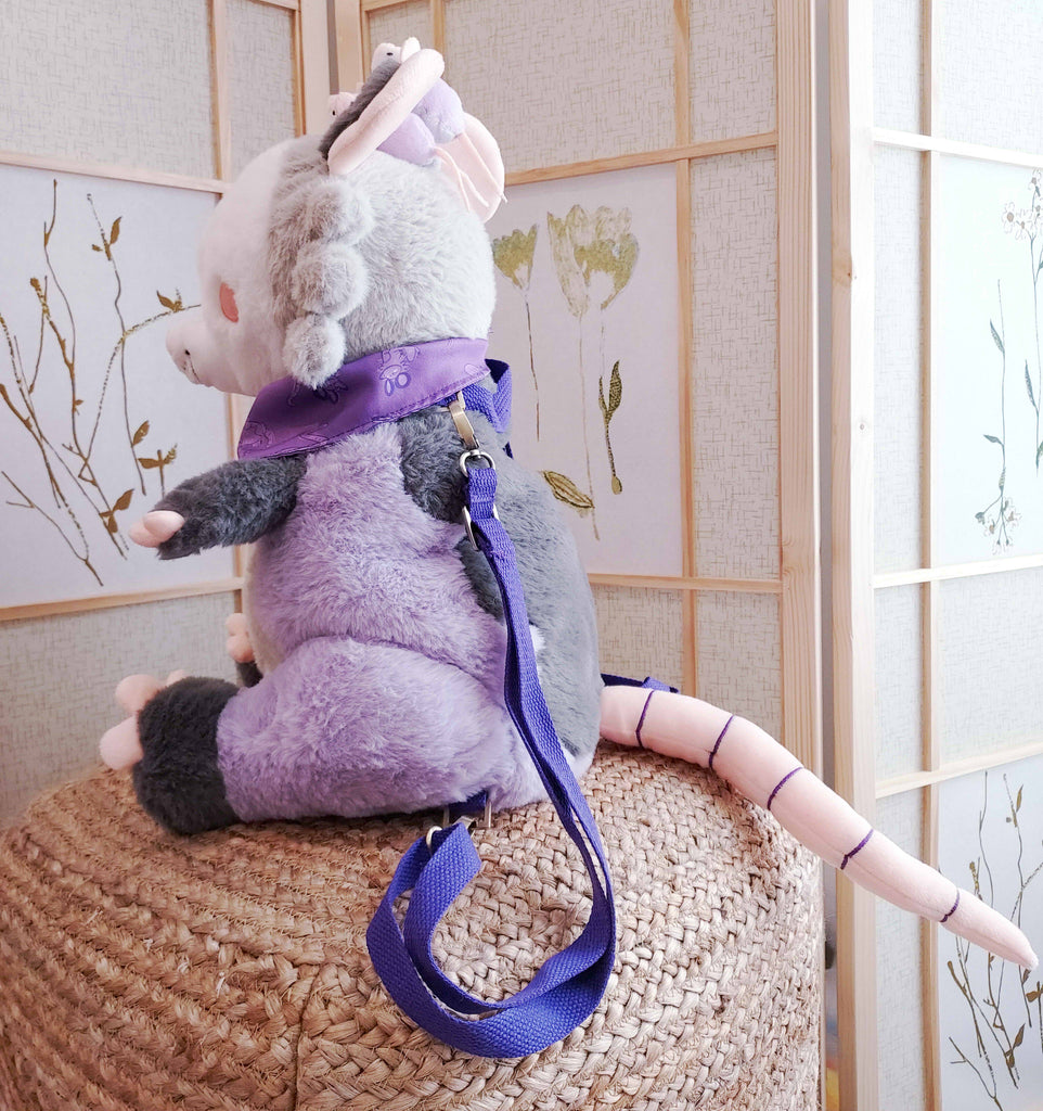 Side view of a plush backpack of Plum the possum wearing a purple bandana, with purple backpack straps
