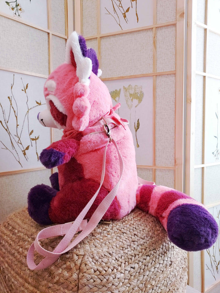 Side view of a plush backpack of Raspberry the red panda wearing a pink bandana, with pink backpack straps
