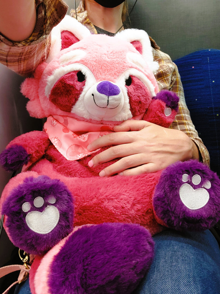 Plush backpack of Raspberry the red panda being held by a person sitting down