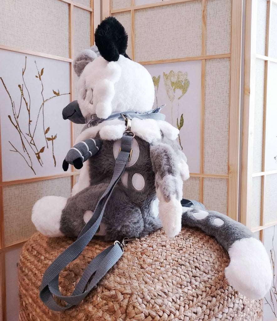 Side view of a plush backpack of Sesame the grey and white gryphon, wearing a light grey bandana, with grey backpack straps