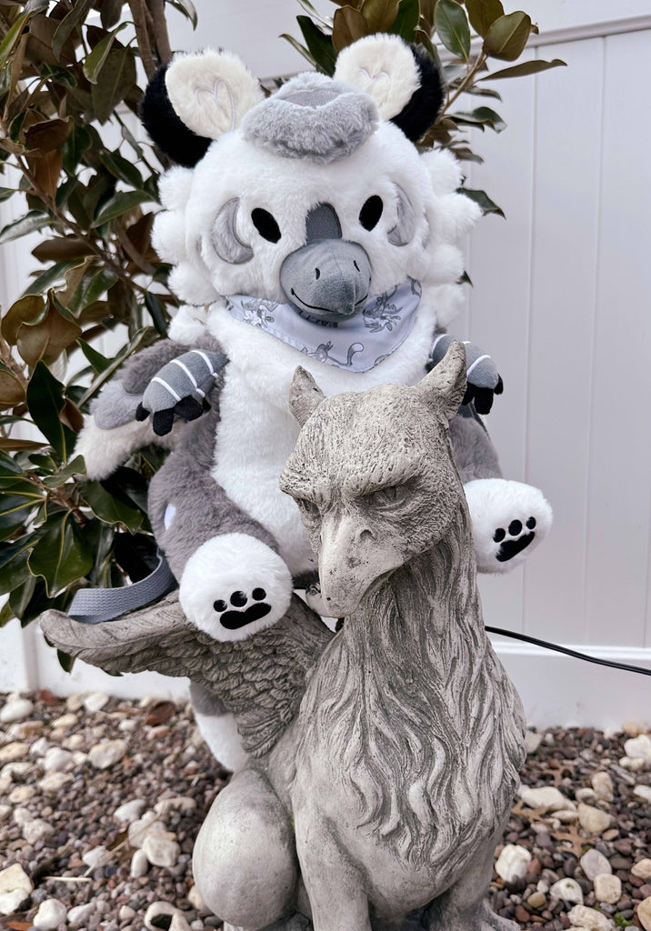 Plush backpack of Sesame the grey and white gryphon sitting atop a stone gryphon statue in the garden